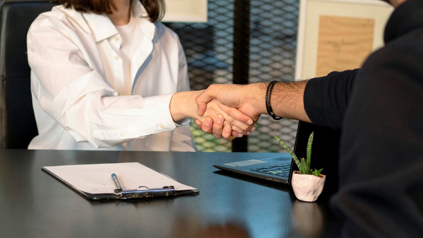 a man and a woman shaking hands in front of a laptop