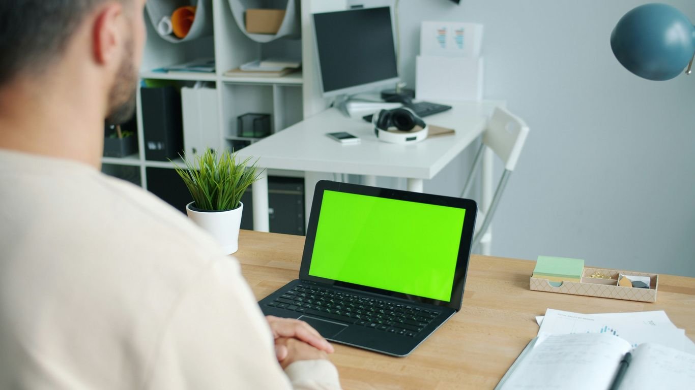 Man working on a laptop with a green screen.