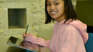 a little girl sitting at a table with a tablet