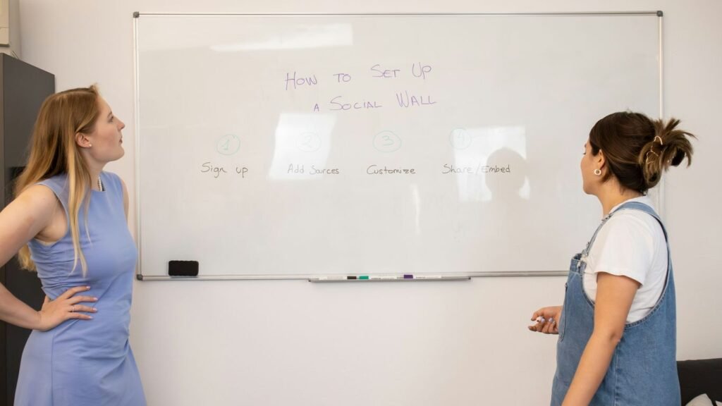 two women standing in front of a white board