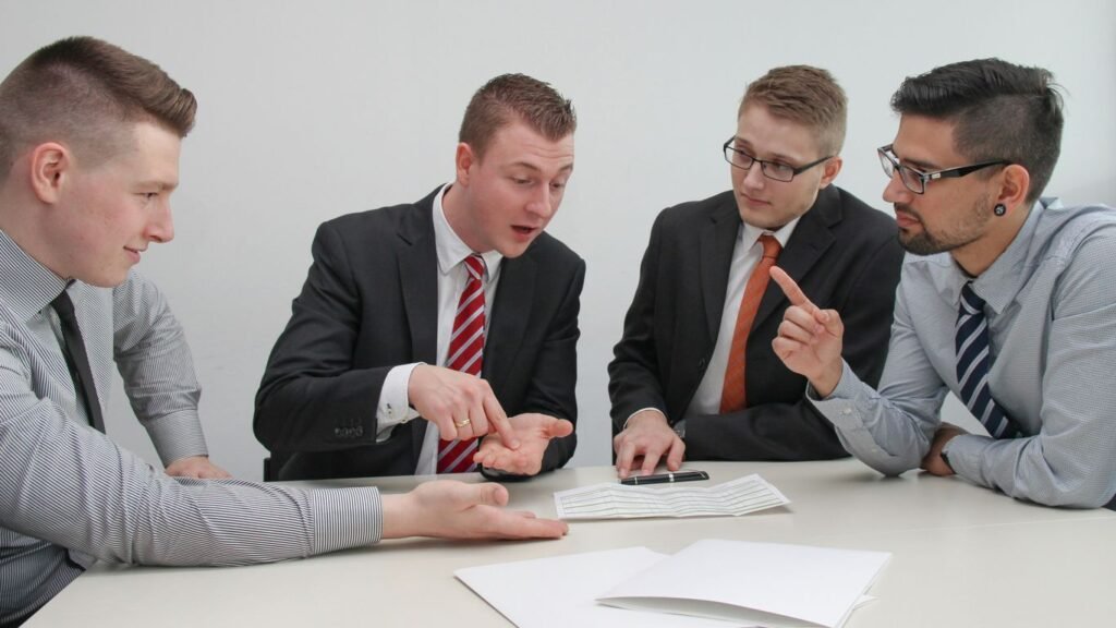 four men sitting at desk talking