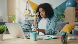 Young woman talking on phone at laptop desk.
