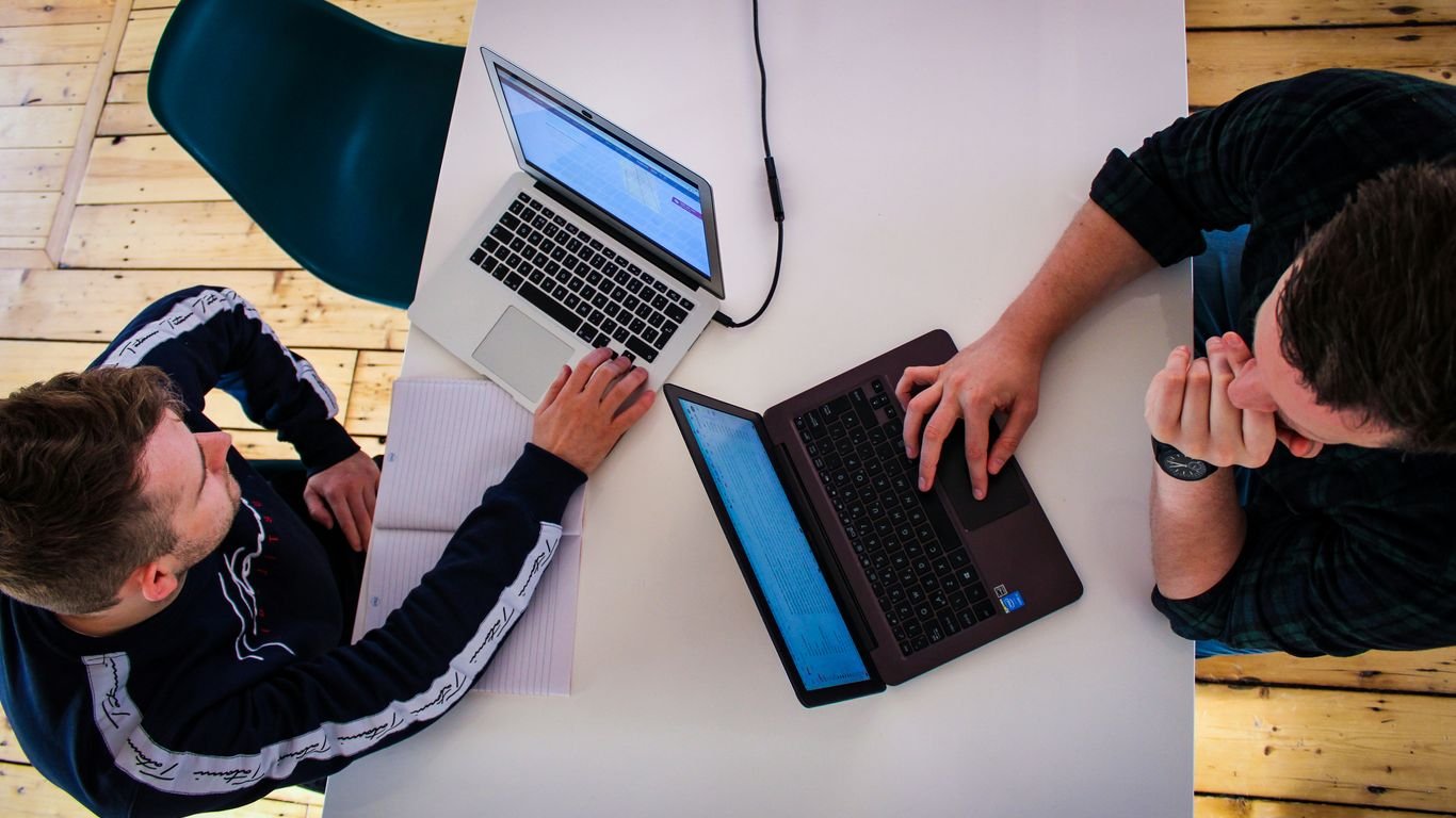 two men sitting at a table working on laptops