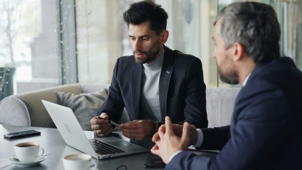 a couple of men sitting at a table with laptops
