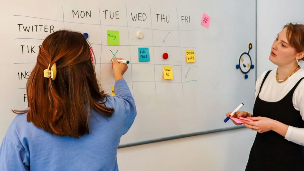 two women writing on a white board with sticky notes