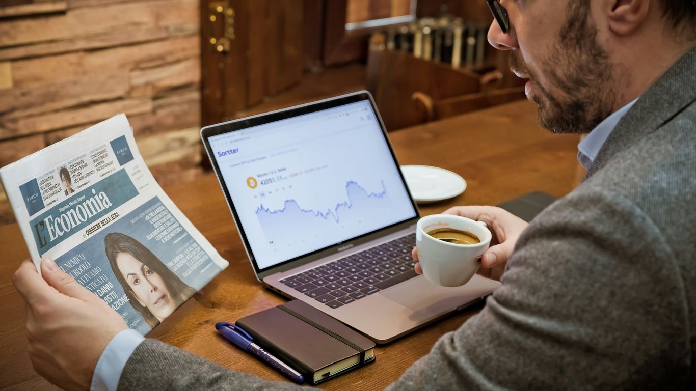 a man sitting at a table with a laptop and a cup of coffee
