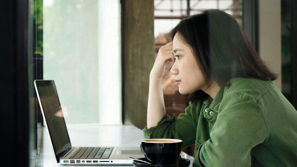woman in green jacket sitting by the table using laptop