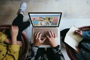 Business owner researching advertising agencies on a laptop and noting questions to ask before hiring