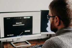 Web designer building an affordable, professional website layout with About Us and Our Mission pages on dual monitors.