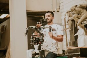 A corporate video producer checks the call sheet and schedule on set while the crew films an interview in the background.