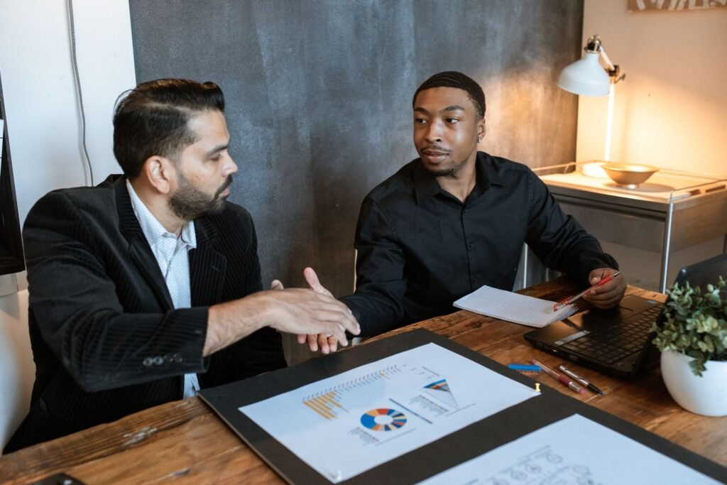 A digital marketing consultant reviewing a campaign spreadsheet with two business owners at a table in a Singapore shophouse office.