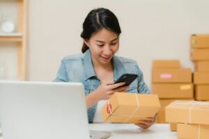 Online store owner packing customer orders beside a laptop, weighing ecommerce site design agency vs DIY