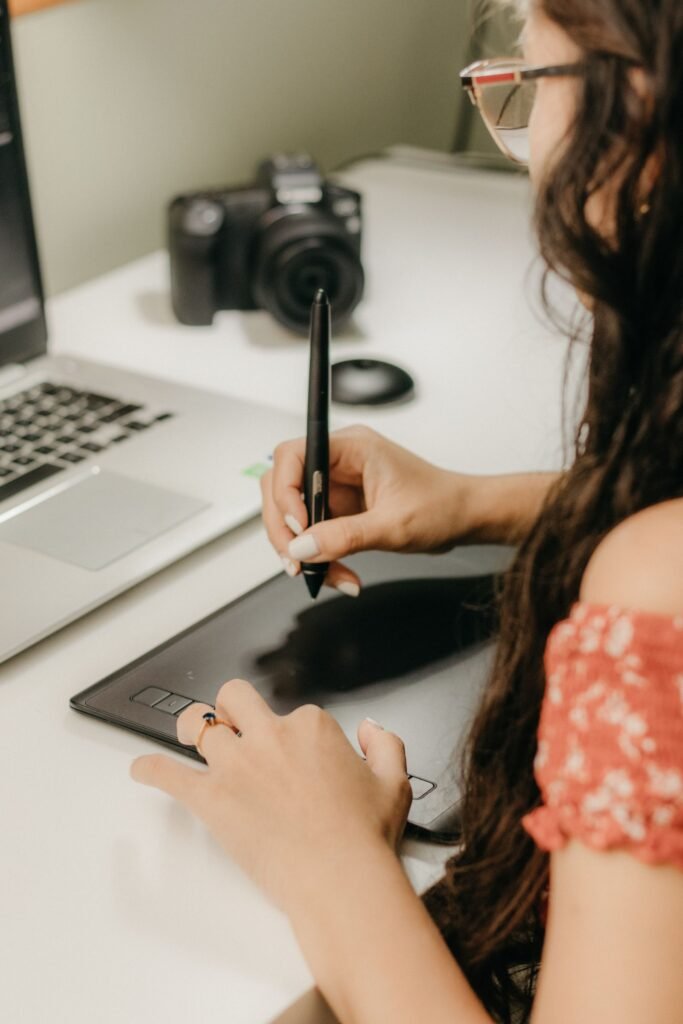 Freelance graphic designer in Singapore working on client branding materials using a graphic tablet and laptop.