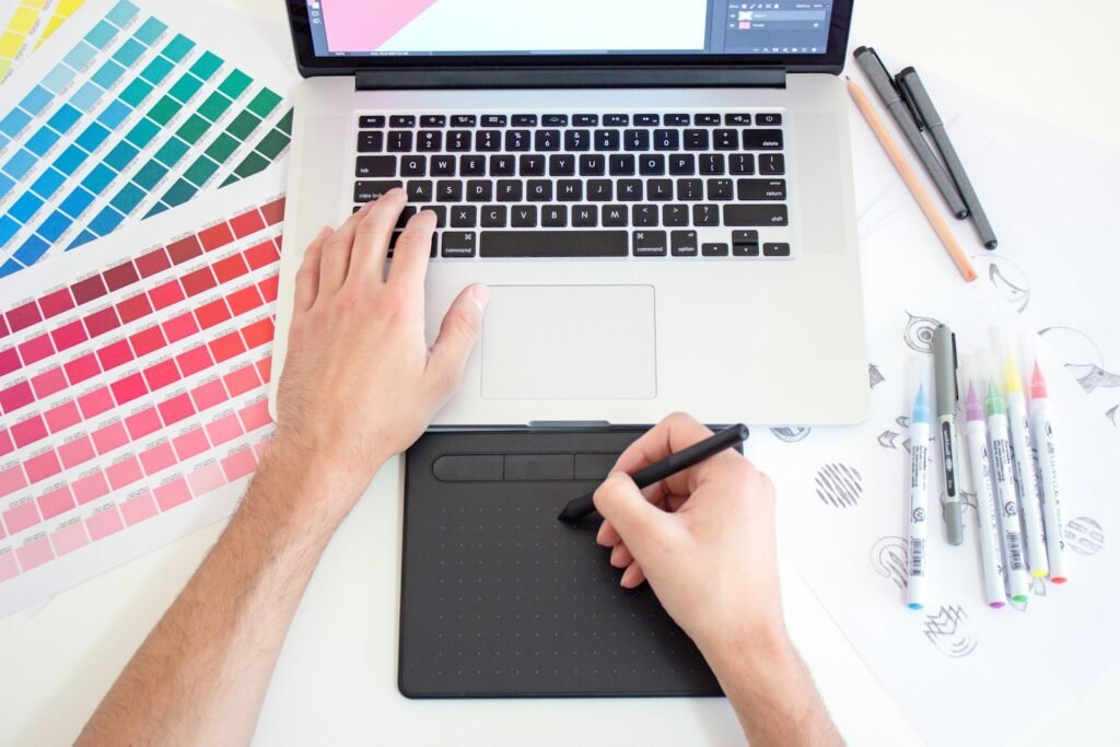 Graphic designer in Singapore working on a drawing tablet beside colour swatches and a laptop