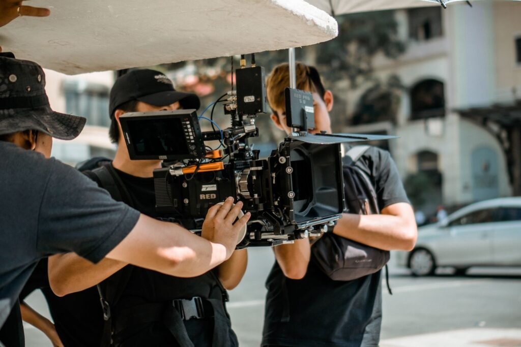 A two-person crew from a local video production company sets up a camera on a Singapore shophouse street while a colleague adjusts a reflector in the afternoon light.