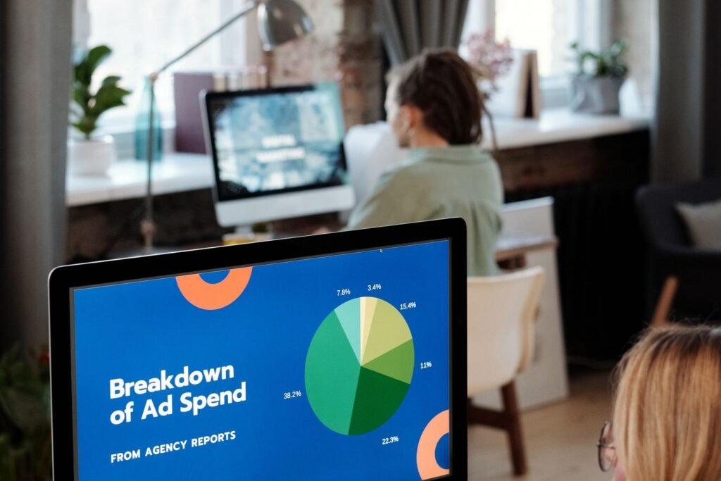 A media buyer at a social media advertising agency compares ad creative variants on one screen against campaign spend figures on another.