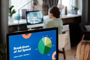 A media buyer at a social media advertising agency compares ad creative variants on one screen against campaign spend figures on another.