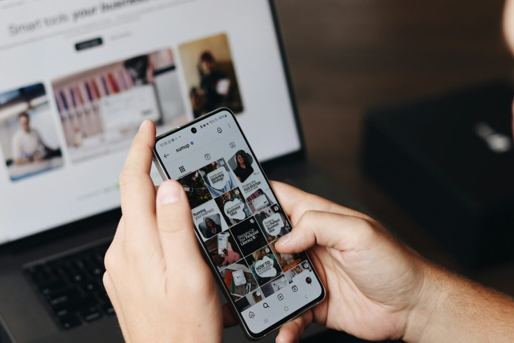 Person browsing a brand social media feed on a smartphone beside a laptop
