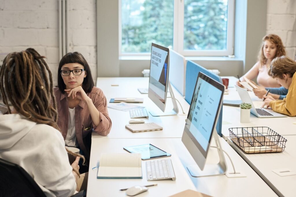 A website development company team reviews a staging build on a monitor while a page template map is pinned to the wall behind them.