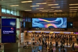 Billboard advertising in Singapore: a large digital screen above the crowd in Changi Airport Terminal 1 arrivals hall
