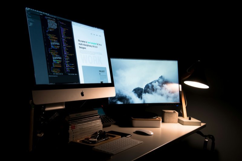 Designer's iMac and monitor showing website code in a dark studio